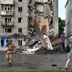 Un residente local pasa junto a un rescatista ucraniano que trabaja fuera de un edificio parcialmente destruido tras un ataque de misiles rusos en Kharkiv, en medio de la invasión militar rusa lanzada sobre Ucrania. | Foto:SERGEY BOBOK / AFP