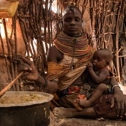 Una mujer amamanta a su hijo dentro de su casa improvisada mientras cocina en la aldea de Parapul, en la zona de Loiyangalani que acoge a las familias afectadas por la prolongada sequía en Marsabit, Kenia. | Foto:Simon Maina / AFP