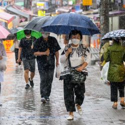 Los peatones pasan por delante de las tiendas que venden productos frescos mientras usan paraguas para resguardarse de la lluvia durante un fuerte aguacero en el mercado de Namseong, en Seúl. | Foto:ANTHONY WALLACE / AFP