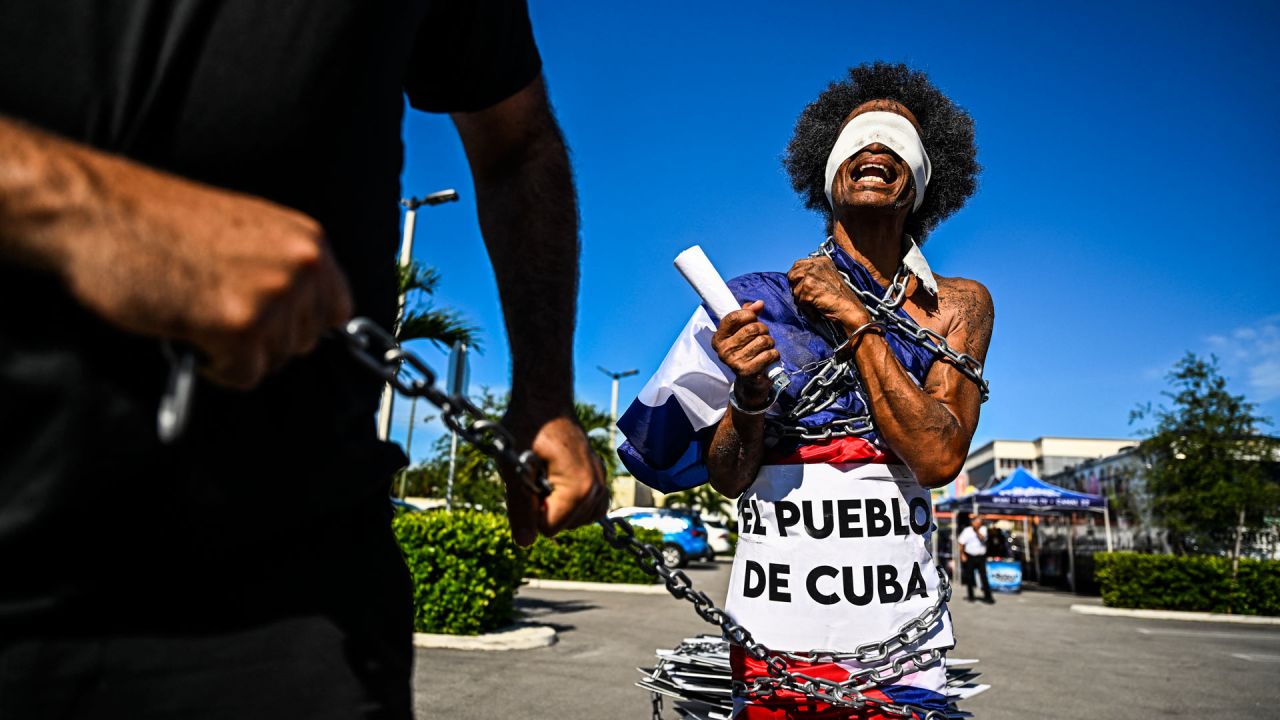 Un hombre atado con una cadena y con los ojos vendados grita consignas mientras marcha por las calles de Miami, Florida, para conmemorar las históricas protestas del año pasado en Cuba. | Foto:CHANDAN KHANNA / AFP