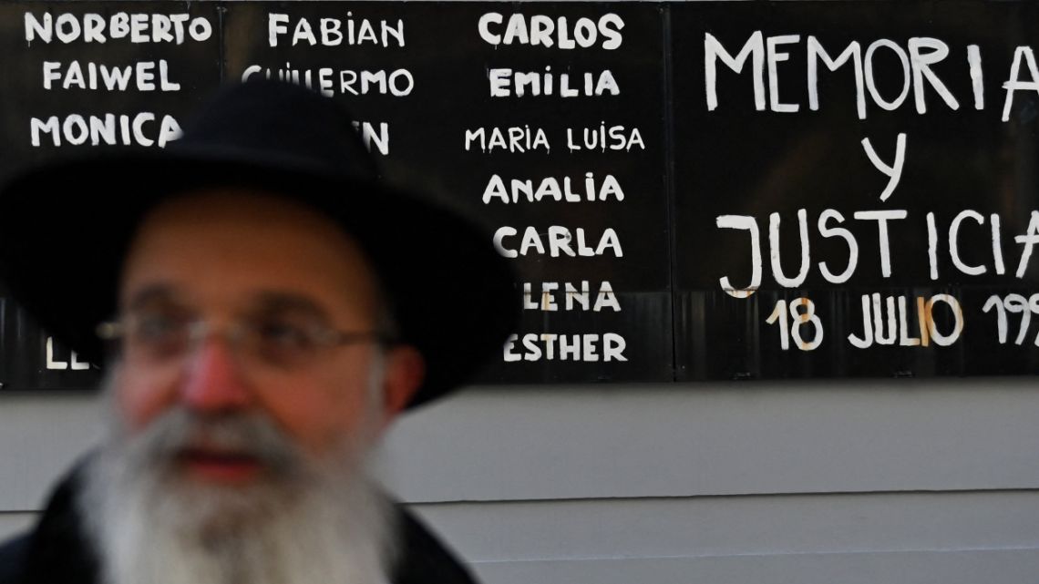 A rabbi is seen in front of a sign reading “Memory and Justice” and names of victims of a bomb attack to the Jewish community centre of the Mutual Israelite Association of Argentina (AMIA) that killed 85 people and injured 300, during its 28th anniversary, in Buenos Aires, Argentina, on July 18, 2022.