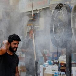 Unos hombres iraquíes se refrescan frente a unos ventiladores en medio de una ola de calor en el centro de Bagdad. | Foto:AHMAD AL-RUBAYE / AFP