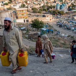 La gente lleva agua potable en contenedores mientras camina por una ladera cerca del cementerio Kart-e-Sakhi en Kabul, Afganistán. | Foto:WAKIL KOHSAR / AFP