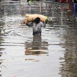 Un vendedor lleva un saco de verduras de hoja vadeando un mercado inundado tras las fuertes lluvias en Lahore, Pakistán. | Foto:ARIF ALI / AFP