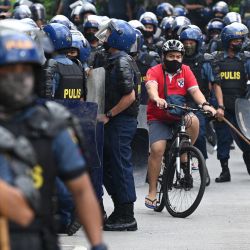 Un ciclista pedalea junto a policías antidisturbios durante una manifestación de protesta de grupos progresistas que coincide con el primer discurso sobre el estado de la nación del presidente filipino Ferdinand Marcos Jr, en Quezon City, en los suburbios de Manila. | Foto:TED ALJIBE / AFP