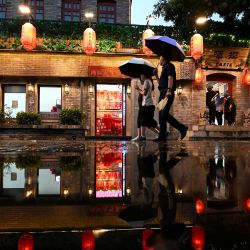 La gente usa paraguas mientras camina en el callejón Nanlouguxiang durante una lluvia en Beijing. | Foto:Noel Celis / AFP
