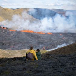 La gente mira la lava que fluye en la escena del volcán que acaba de entrar en erupción en Grindavik, Islandia. | Foto:Jeremie Richard / AFP