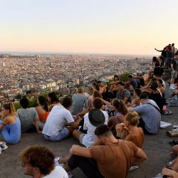 La gente se reúne para ver la puesta de sol en la cima de una colina con vistas al horizonte de Barcelona. | Foto:PAU BARRENA / AFP