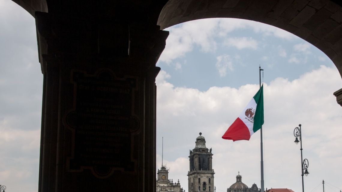 A taxi cab passes in front of the Mexican flag flying at the Plaza de la Constitucion (Zocalo) in Mexico City, Mexico, on Friday, April 13, 2018. Mexico's peso extended losses for a third day amid profit-taking outflows as the currency failed to stay strong past 18.00 key level.
