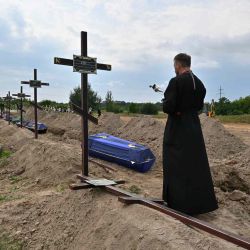 Un sacerdote ortodoxo sirve en las tumbas de civiles no identificados durante su funeral en un cementerio local en la ciudad de Bucha, región de Kyiv. Sergei SUPINSKY / AFP. | Foto:AFP