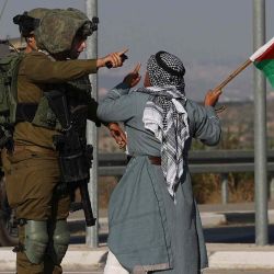 Un manifestante palestino que lleva una bandera nacional se enfrenta a un miembro de las fuerzas de seguridad israelíes durante una manifestación contra los asentamientos judíos, al este de la ciudad ocupada de Qalqilia, en Cisjordania. JAAFAR ASHTIYEH / AFP. | Foto:AFP
