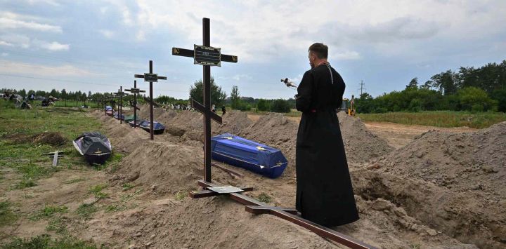 Un sacerdote ortodoxo sirve en las tumbas de civiles no identificados durante su funeral en un cementerio local en la ciudad de Bucha, región de Kyiv. Sergei SUPINSKY / AFP.
