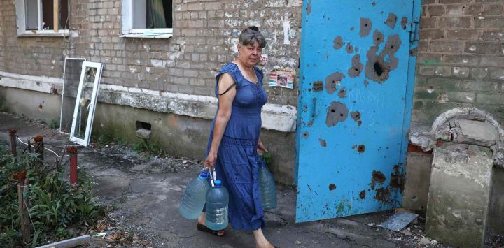 Una mujer lleva botellas de agua mientras pasa frente a un edificio dañado en la ciudad de Avdiivka, región de Donetsk, en medio de la invasión militar rusa de Ucrania. Anatolii Stepanov / AFP.
