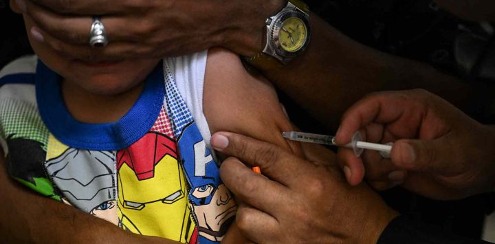 Un niño acompañado de su padre recibe una dosis de la vacuna contra el sarampión y la rubéola por parte de personal médico en un centro de salud comunitario en el barrio Lidice de Caracas. Yuri CORTEZ / AFP.