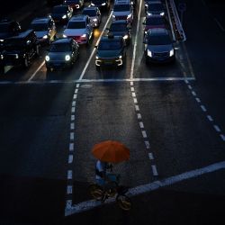 Una mujer con un paraguas se refugia de la lluvia mientras conduce una bicicleta compartida que cruza una calle en Pekín, China. | Foto:Wang Zhao / AFP