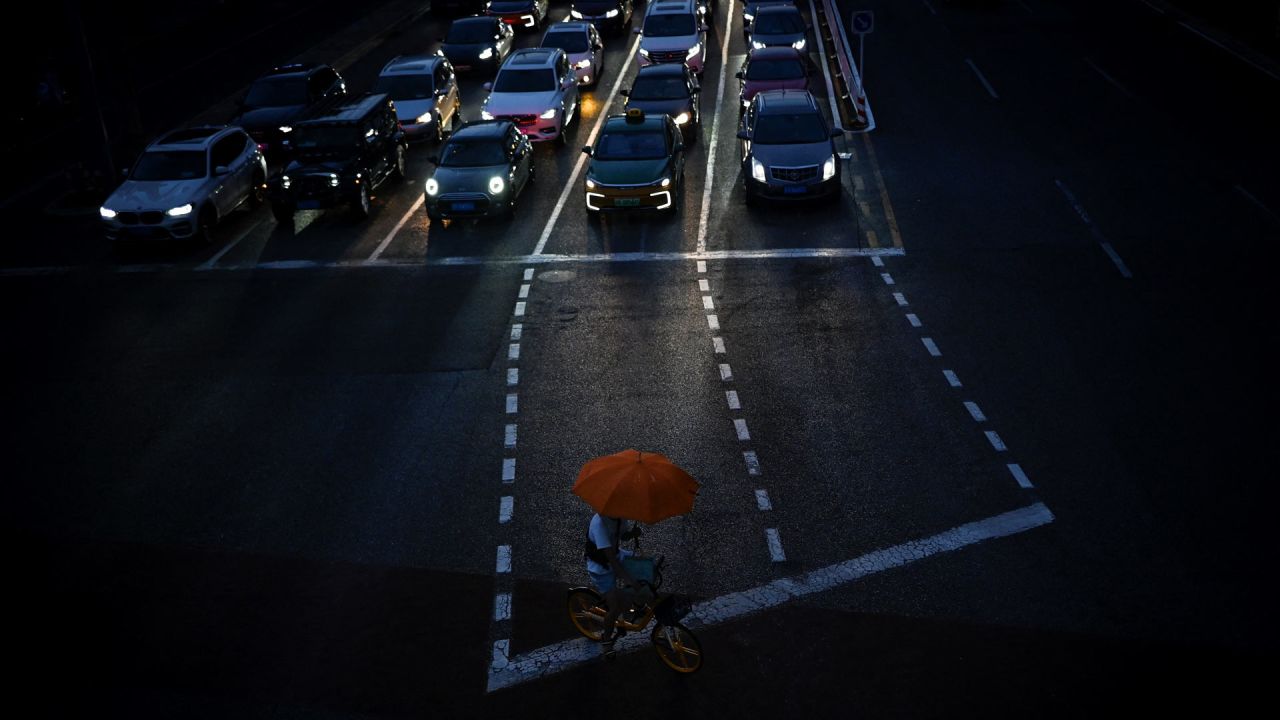 Una mujer con un paraguas se refugia de la lluvia mientras conduce una bicicleta compartida que cruza una calle en Pekín, China. | Foto:Wang Zhao / AFP
