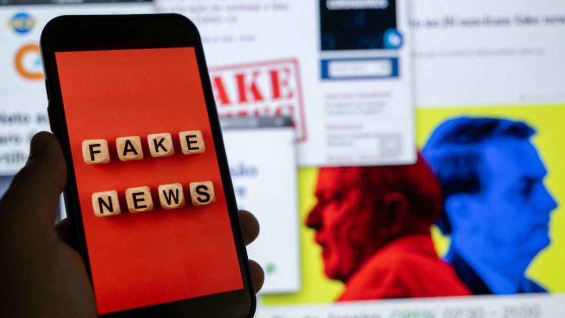 This illustration picture shows a smart phone screen displaying the phrase "Fake News" in front of a desktop screen showing several news and research reports about fake news and disinformation related to the upcoming Brazilian presidential election.