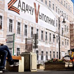 Un hombre se sienta junto a una pancarta que muestra las letras Z y V, insignias tácticas de las tropas rusas en Ucrania, y en la que se lee "¡Cumpliremos la tarea!" en el edificio administrativo del Teatro Bolshói, en el centro de Moscú. | Foto:ALEXANDER NEMENOV / AFP