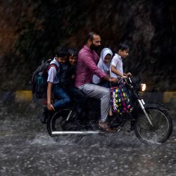 Un hombre conduce una motocicleta con niños como pasajero a lo largo de una carretera durante las fuertes lluvias en Karachi, Pakistán. | Foto:Asif Hassan / AFP