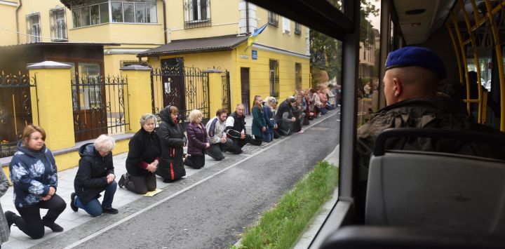 Personas arrodilladas rinden respeto al militar ucraniano Volodymyr Haysler mientras su féretro es transportado en autobús al cementerio de Lychakiv, en la ciudad occidental ucraniana de Lviv, en medio de la invasión rusa de Ucrania.