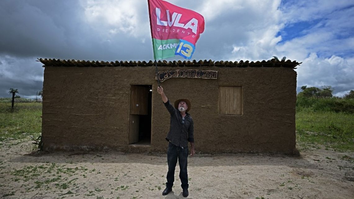 Eraldo dos Santos, cousin of Brazil's presidential candidate for the leftist Workers' Party (PT) and former president (2003-2010) Luiz Inácio Lula da Silva, waves a flag outside a replica of the long-collapsed shack where Lula was born 76 years ago outside the town of Caetés, in Pernambuco state, on September 1, 2022. 