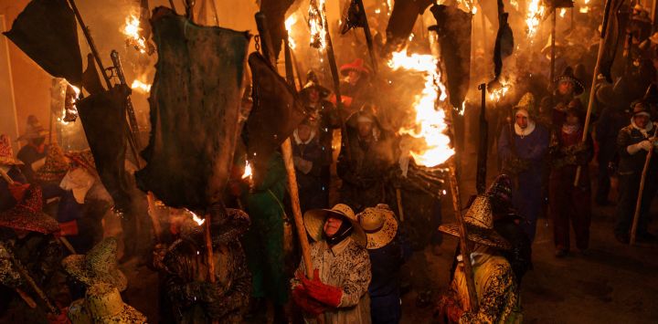 Participantes con gorro y guantes para protegerse de las quemaduras llevan antorchas hechas con odres en llamas, durante la procesión de antorchas de "El Vitor", en Mayorga, España.