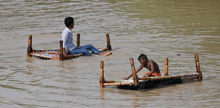 Unas personas se sientan en un charpai, un lecho tradicional, en una zona inundada después de que el nivel del agua del río Yamuna aumentara debido a las recientes lluvias, en Nueva Delhi, India.