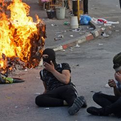 Manifestantes palestinos sentados cerca de neumáticos en llamas en medio de enfrentamientos con las fuerzas de seguridad israelíes en la ciudad de Hebrón, en la Cisjordania ocupada. | Foto:HAZEM BADER / AFP