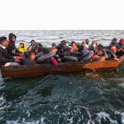 Migrantes del África subsahariana sentados en una embarcación improvisada que estaba siendo utilizada para dirigirse clandestinamente hacia la costa italiana, mientras son encontrados por las autoridades tunecinas a unas 50 millas náuticas en el mar Mediterráneo frente a la costa de la ciudad central de Túnez, Sfax. | Foto:FETHI BELAID / AFP
