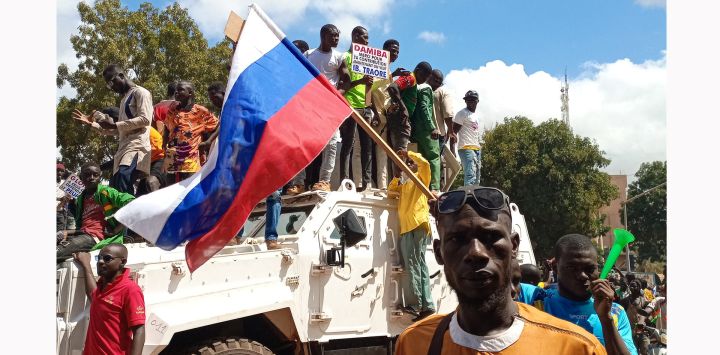 Los manifestantes se sitúan encima de un vehículo blindado de Unitend Nation mientras se manifiestan con una bandera rusa en Uagadugú. - Las fuerzas de seguridad dispararon gases lacrimógenos para dispersar a los manifestantes frente a la embajada de Francia en la capital de Burkina Faso, mientras los disturbios se mantienen a fuego lento en la empobrecida nación de África Occidental tras la afirmación de un segundo golpe de Estado este año.