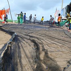 Hijos de pescadores senegaleses arreglan las redes de pesca en la costa de Saint Louis, cerca de una plataforma donde se está explotando un importante descubrimiento de gas en alta mar, en el norte de Senegal. | Foto:SEYLLOU / AFP