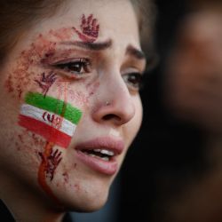 Una manifestante con una bandera iraní y las manos rojas pintadas en la cara asiste a una concentración de apoyo a las protestas iraníes, tras la muerte de la iraní Mahsa Amini en Irán. | Foto:JULIEN DE ROSA / AFP
