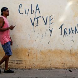 Un hombre pasa junto a un grafiti que dice "Cuba vive y trabaja" en La Habana. | Foto:YAMIL LAGE / AFP