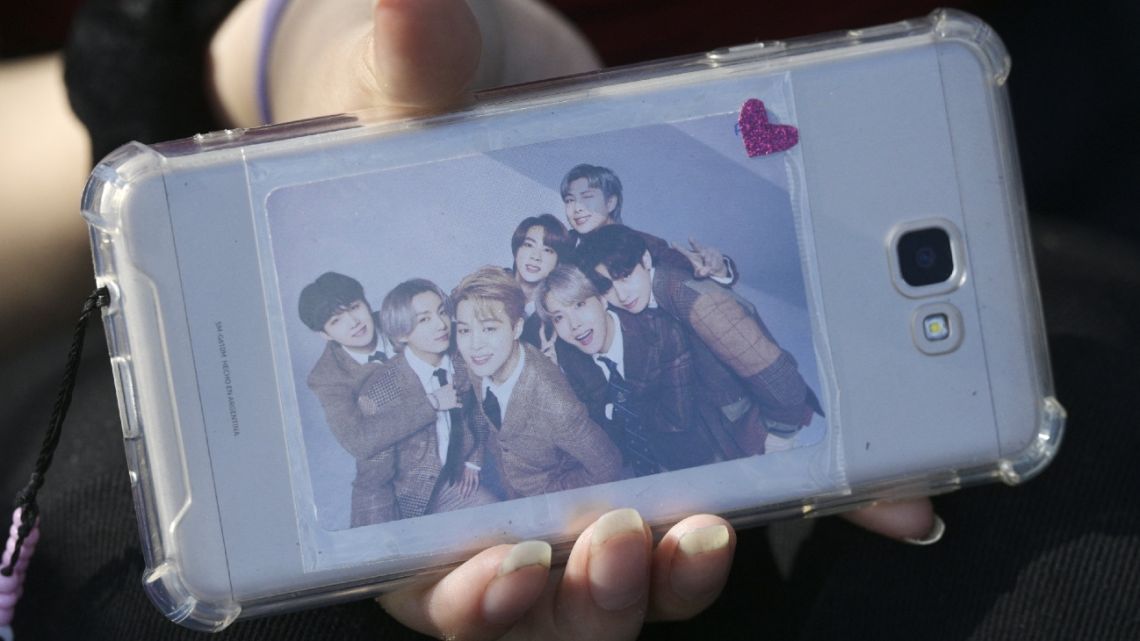A fan of the South Korean band BTS shows her cellphone covered with a picture of the band members while camping near River Plate's Monumental stadium to attend Coldplay's Friday concert in Buenos Aires, on October 26, 2022.