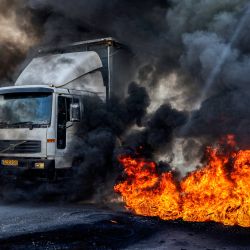 Un camión que se dirige a Nablus pasa por delante de unos neumáticos en llamas en el puesto de control de Hawara, al sur de la ciudad palestina en la Cisjordania ocupada, que fueron incendiados por manifestantes palestinos que exigían la reapertura de las carreteras en torno a la ciudad cerrada de Nablus, que ha estado bajo bloqueo militar desde el 11 de octubre después de que hombres armados palestinos mataran a un soldado israelí cerca del asentamiento de Shavei Shomron. | Foto:JAAFAR ASHTIYEH / AFP