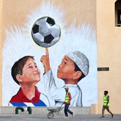 Un trabajador empuja una carretilla junto a un mural en Doha, antes del torneo de fútbol de la Copa Mundial de la FIFA Qatar 2022. | Foto:GABRIEL BOUYS / AFP