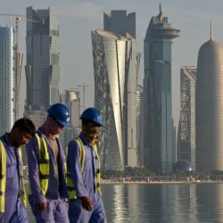 Los trabajadores tienen como telón de fondo el horizonte de Doha mientras caminan por el paseo marítimo de Corniche en Doha, Qatar. | Foto:MARIANA SUAREZ / AFP