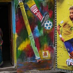 Una mujer se asoma a la puerta de una casa decorada con un póster del futbolista brasileño Neymar Jr y murales de apoyo a la selección de fútbol de Brasil para que triunfe en el Mundial de Qatar 2022, en Calcuta, India. | Foto:DIBYANGSHU SARKAR / AFP