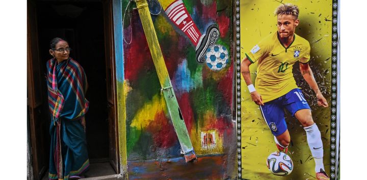 Una mujer se asoma a la puerta de una casa decorada con un póster del futbolista brasileño Neymar Jr y murales de apoyo a la selección de fútbol de Brasil para que triunfe en el Mundial de Qatar 2022, en Calcuta, India.