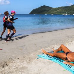 En la foto se ve una mujer en la playa mientras las competidoras corren durante una carrera de atletismo como parte de la competición multideportiva "Raid des Alizes", exclusivamente femenina, en la isla caribeña francesa de Martinica. | Foto:CHARLY TRIBALLEAU / AFP