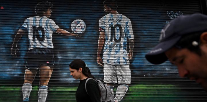 La gente pasa por delante de un mural del artista Causi que representa a las estrellas del fútbol argentino Lionel Messi y el fallecido Diego Maradona en Buenos Aires.
