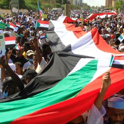 Manifestantes sudaneses despliegan una bandera nacional gigante, mientras marchan frente a la sede de la ONU en el distrito de Manshiya de la capital Jartum. | Foto:Ebrahim Hamid / AFP
