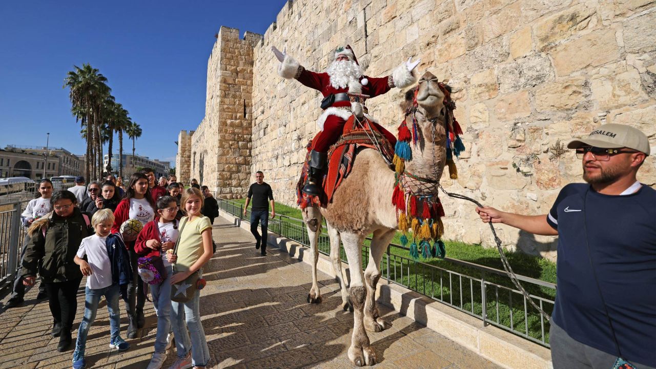 El palestino Issa Kassissieh, vestido de Papá Noel, monta un camello en la Puerta de Jaffa, en la Ciudad Vieja de Jerusalén, unas semanas antes de la próxima fiesta de Navidad. | Foto:AHMAD GHARABLI / AFP