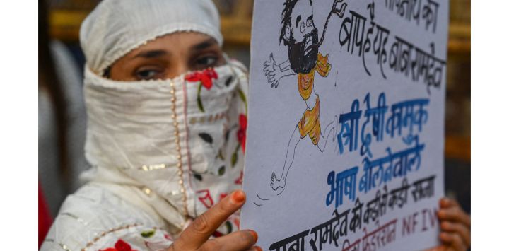 Un activista mira desde detrás de un cartel con una caricatura del autoproclamado gurú indio del yoga Baba Ramdev, durante una protesta contra él en Bombay, India.