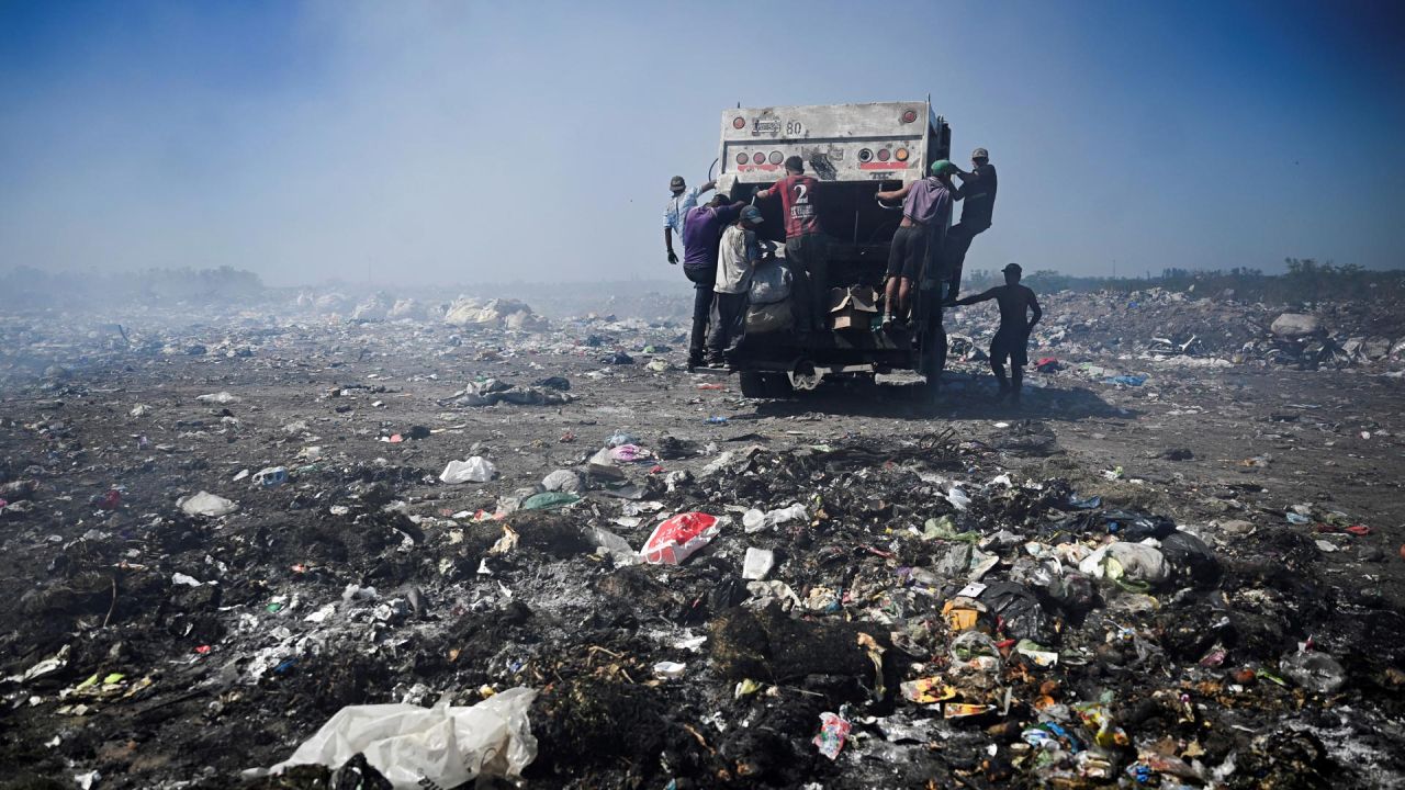 Recicladores se cuelgan de un camión de basura, en el vertedero de Luján, Argentina. - Decenas de personas buscan entre la basura objetos reciclables que venden para el sustento de sus hogares y como forma de hacer frente a la crisis económica del país. El vertedero de Luján, el más grande a cielo abierto de Argentina, se transformará en un centro medioambiental, poniendo fin a años de contaminación, insalubridad y también a la forma de ganarse la vida de estos recicladores. | Foto:LUIS ROBAYO / AFP