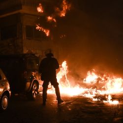 Un policía antidisturbios junto a una hoguera que estalló durante los enfrentamientos durante una manifestación contra la violencia policial, con motivo del 14º aniversario del atropello mortal de un adolescente por la policía en 2008 en Tesalónica, Grecia. | Foto:SAKIS MITROLIDIS / AFP