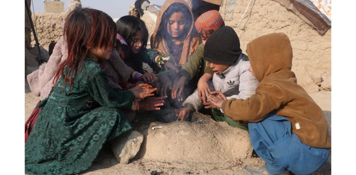 Niños afganos desplazados internos se calientan alrededor de un fuego fuera de su casa temporal de barro en las afueras de la provincia de Herat.