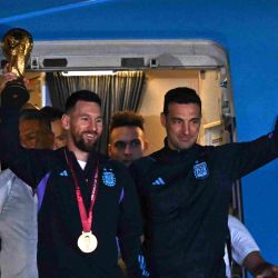 Lionel Messi sostiene el Trofeo de la Copa Mundial de la FIFA junto al entrenador de Argentina Lionel Scaloni mientras bajan de un avión a su llegada al Aeropuerto Internacional de Ezeiza después de ganar el torneo de la Copa Mundial Qatar 2022 en Ezeiza, provincia de Buenos Aires. | Foto:LUIS ROBAYO / AFP