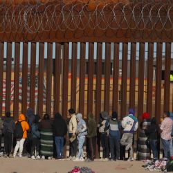 Migrantes hacen cola en el muro fronterizo para ser recibidos por agentes de la Patrulla Fronteriza tras cruzar el río Bravo desde Ciudad Juárez, estado de Chihuahua, México, hasta El Paso, Texas, Estados Unidos. | Foto:Herika Martínez / AFP