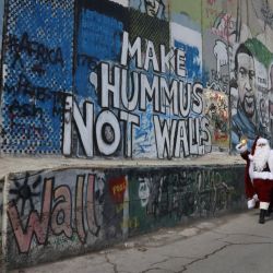 Un hombre vestido con un traje de Papá Noel camina junto al muro de separación de Israel en la ciudad bíblica de Belén, en Cisjordania, durante la Navidad. | Foto:HAZEM BADER / AFP